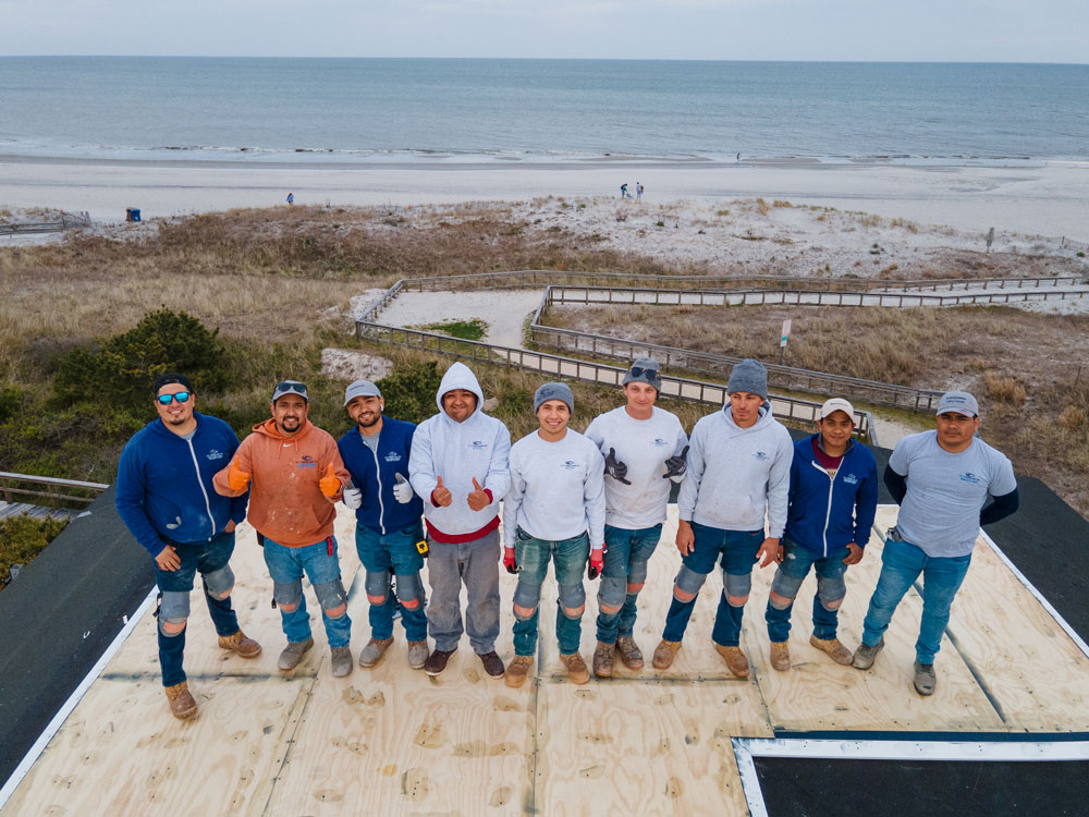 Members of the OC Fiberglass team posing for a photo on a roof with the beach and ocean in the background.