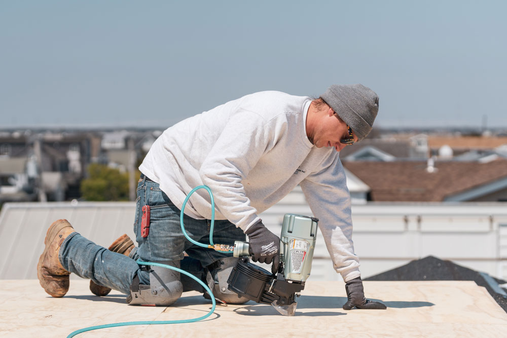 A man wearing sunglasses using power tools whie working on a roof.