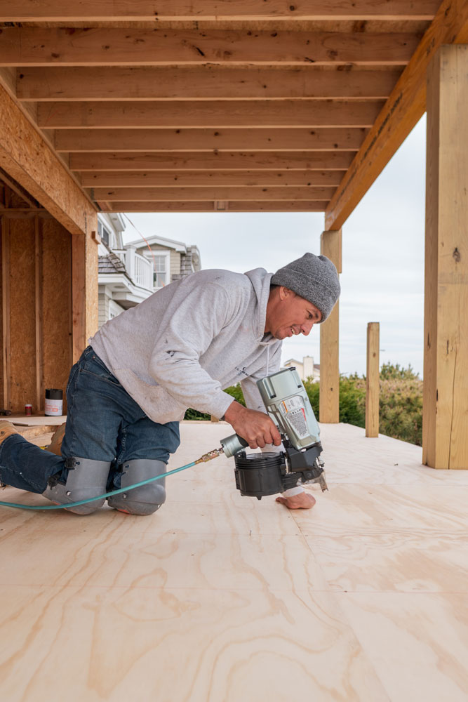 A smiling man using power tools while working on a house.