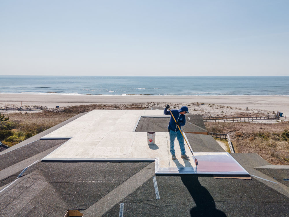A member of the OC Fiberglass team working on a roof with the ocean in the background.