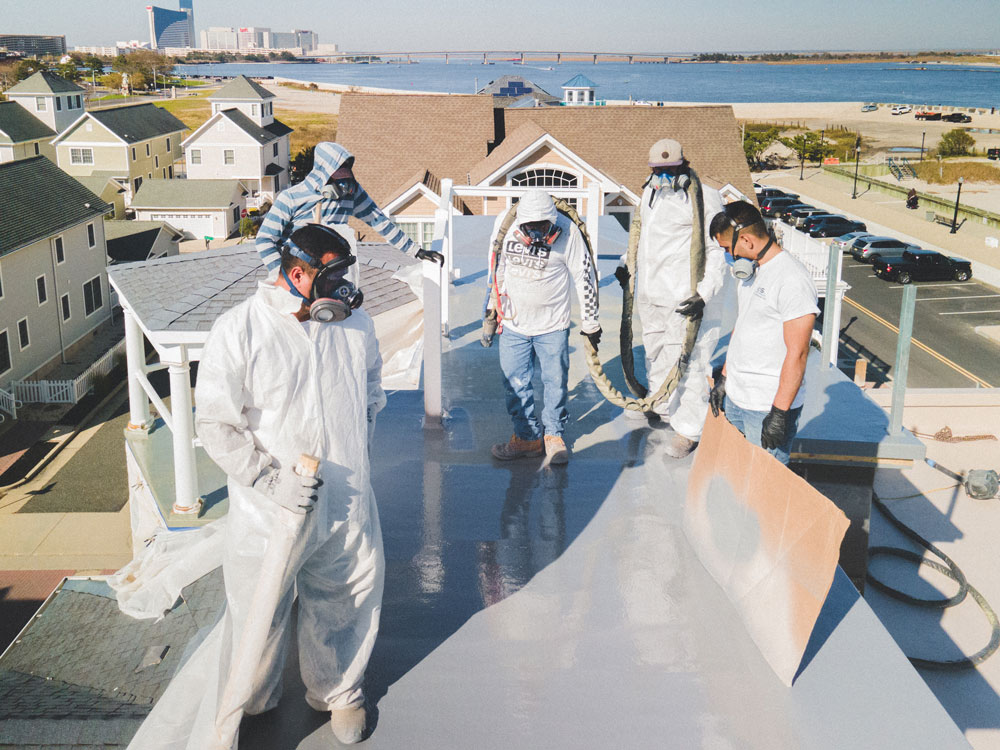 Five team members with masks applying poly to a roof.
