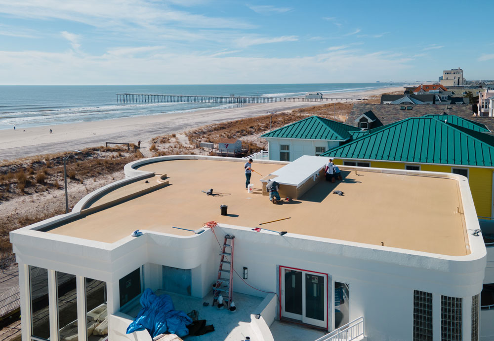 A technician painting the roof of a home that's located near the beach.
