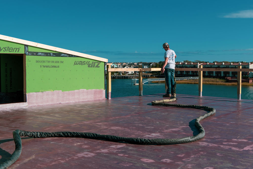 A man using a hose on a roof near a body of water.