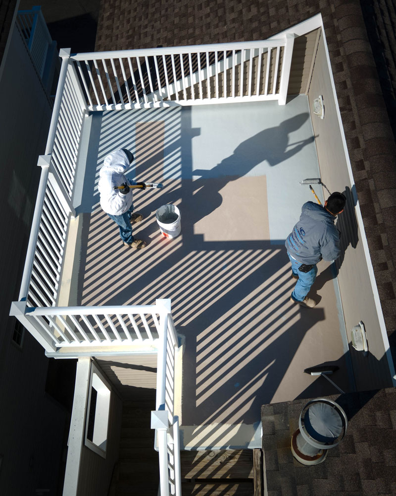 Two team members in the process of painting a roof deck.